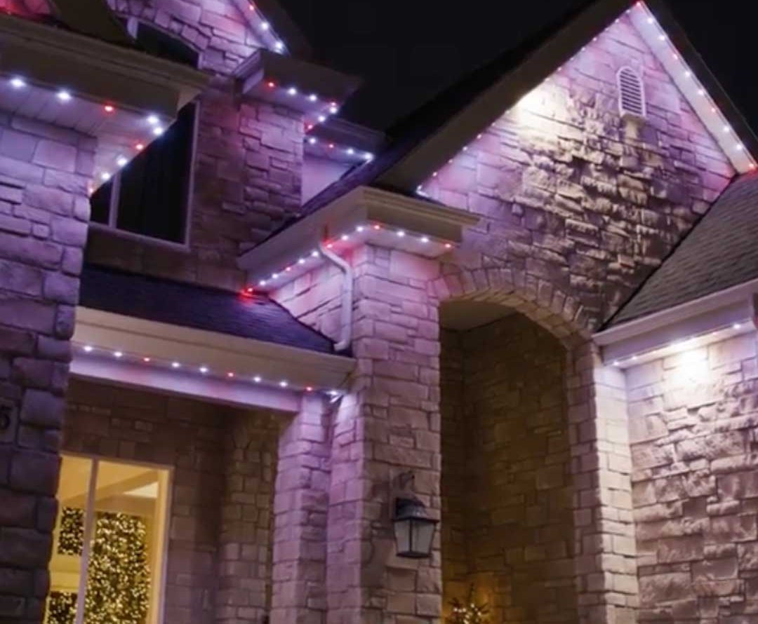 Permanent LED roofline lighting on a stone home, lit in pink and white